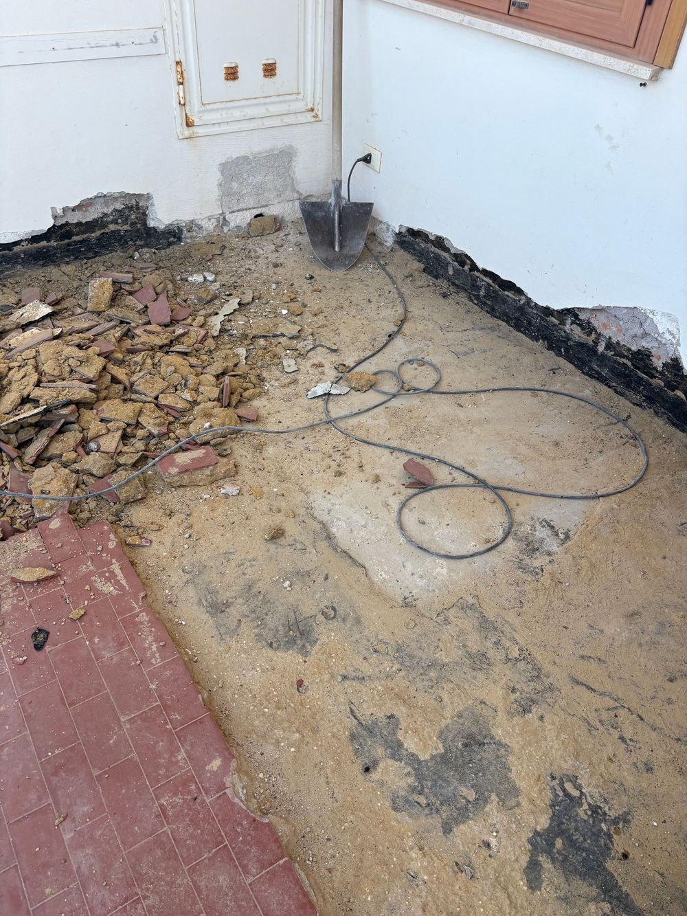 Detriti edili e sporcizia grezzi su un angolo del tetto con cavi neri vicino a un muro e una porta