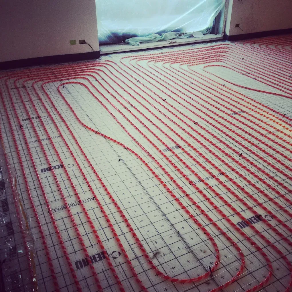In una stanza non rifinita, tubi rossi per il riscaldamento a pavimento sono disposti a spirale su un pavimento a griglia.