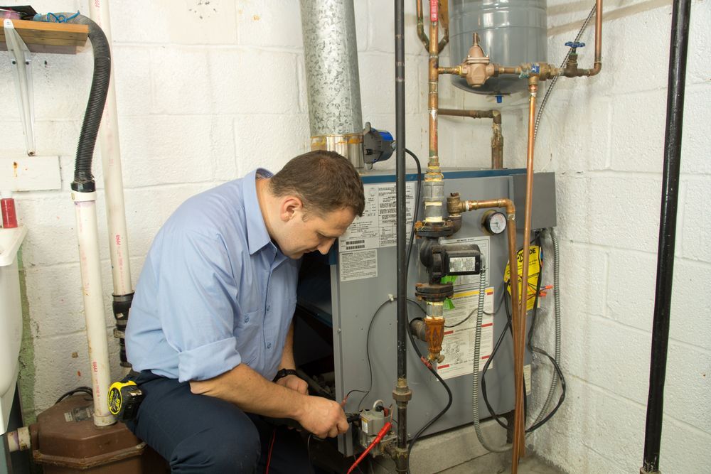 Man in Blue Shirt Works on Furnace in a Basement — Zac Rennick Plumbing in Wellington, NSW