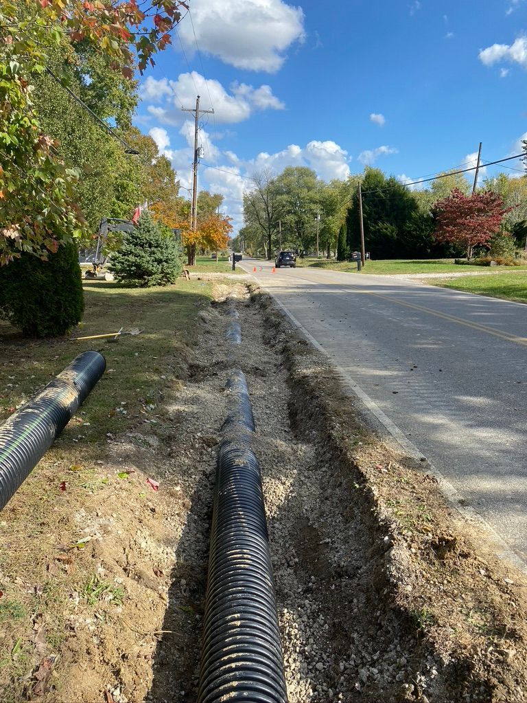 Trench dug alongside a road with a large black drainage pipe ready for installation