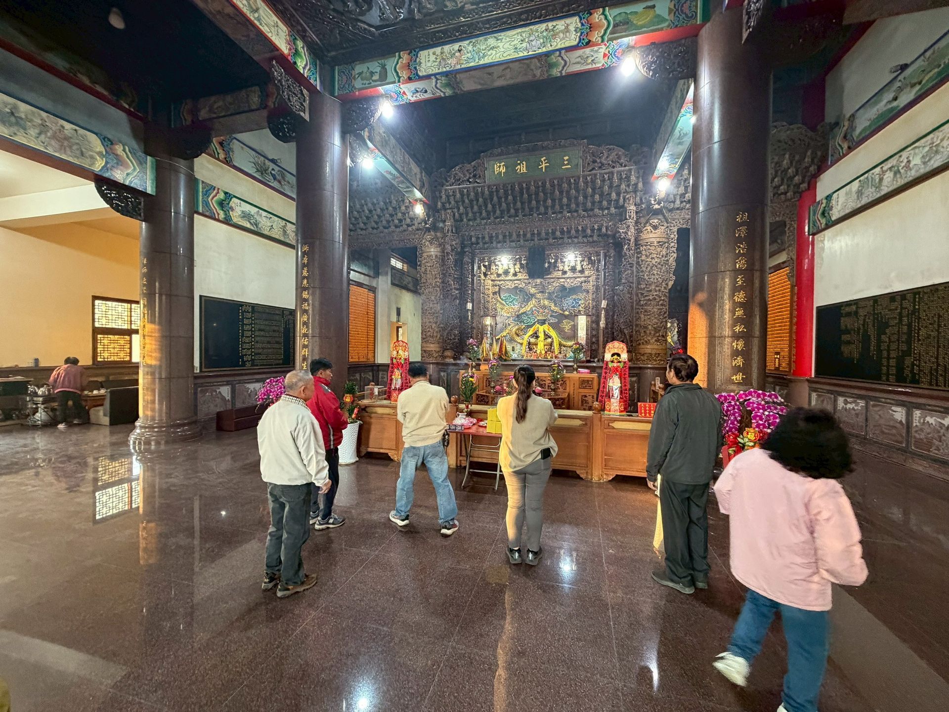 寺廟裡，人們面向祭壇。可以看到精美的雕刻、柱子和光潔的地板。