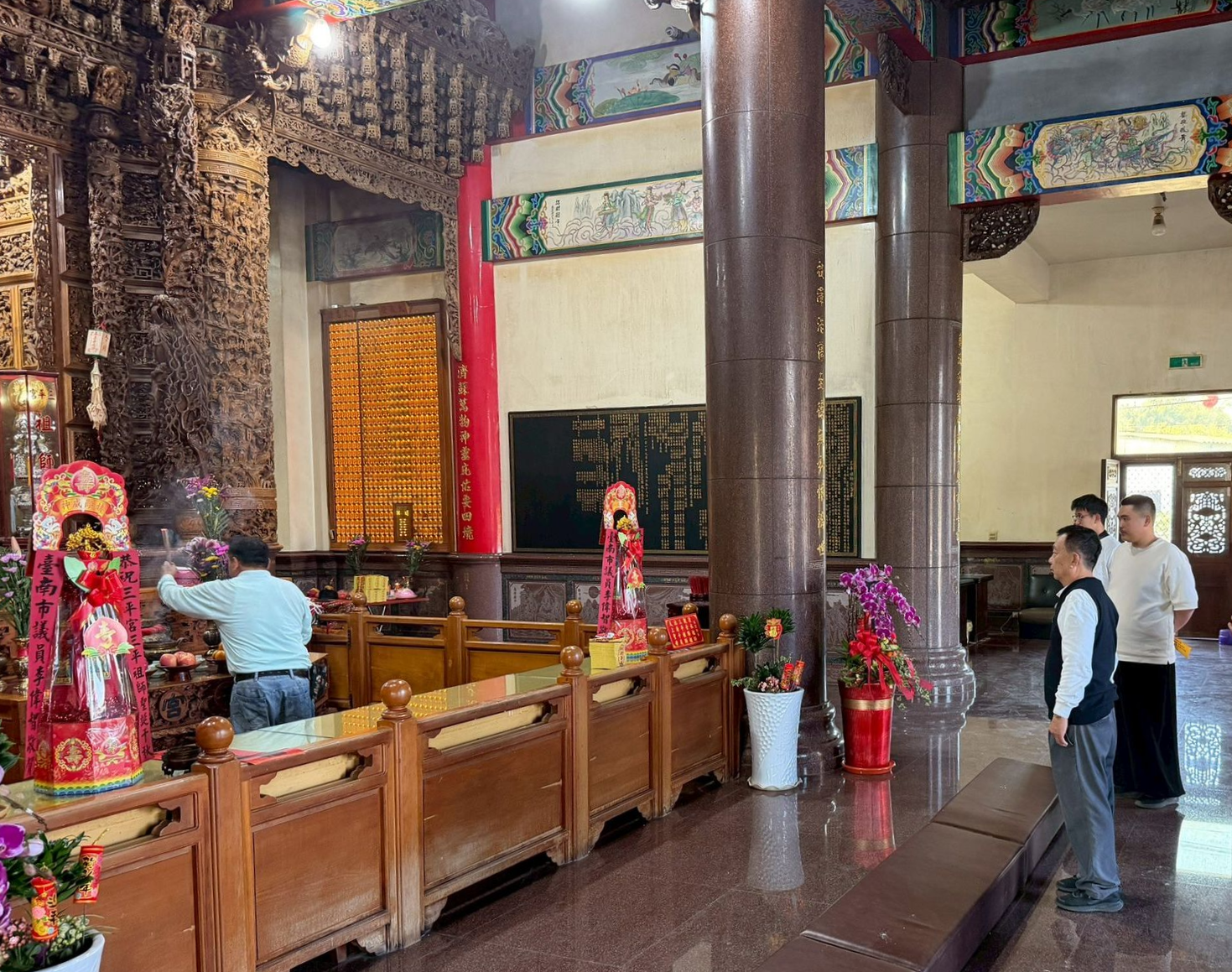 寺廟內部：人們在祈禱，裝飾華麗，有紅色和金色的雕像，還有木製欄桿和柱子。