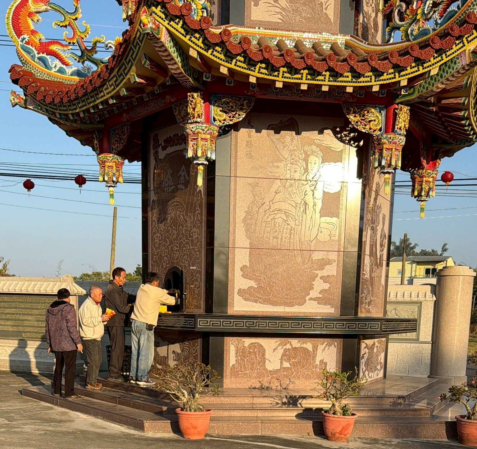 人們在一座有多層屋頂和雕刻柱子的寺廟建築中，將物品放在平台上。