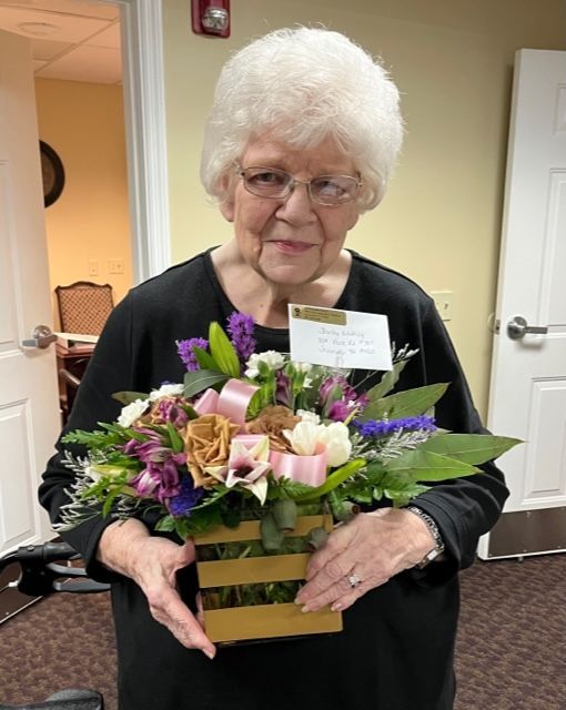 An elderly woman is holding a basket of flowers in her hands.