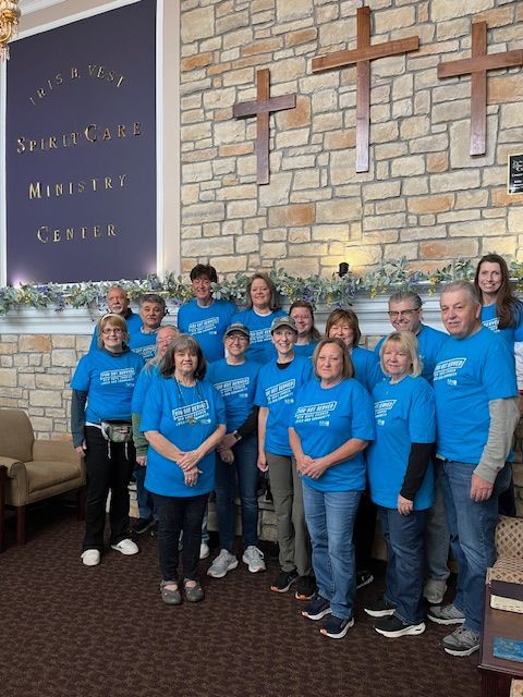 A group of people wearing blue shirts are posing for a picture in front of a stone wall.