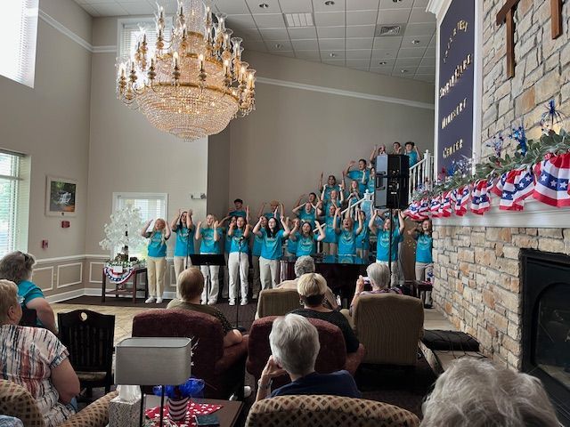 A group of people are sitting in a living room watching a choir perform.