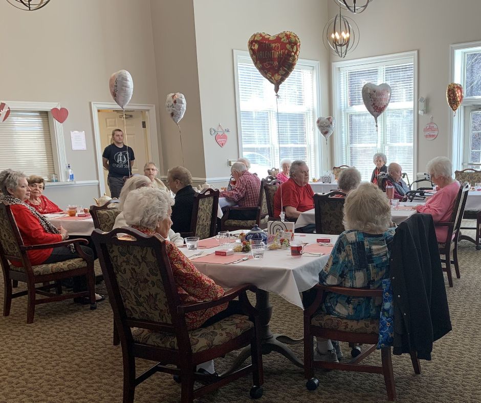 A group of people are sitting at tables in a room with balloons in the shape of hearts.