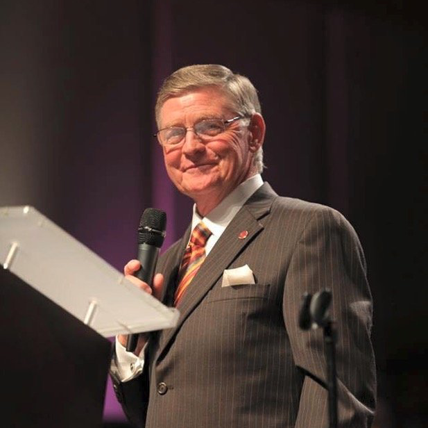 A man in a suit stands at a podium holding a microphone