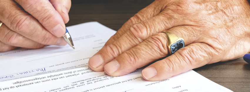 A person with a ring on their finger is writing on a piece of paper.