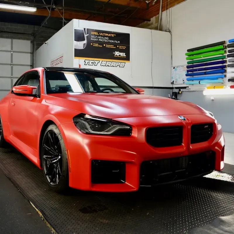Red sports sedan in a garage, with a matte red finish and black wheels on a dynamometer.