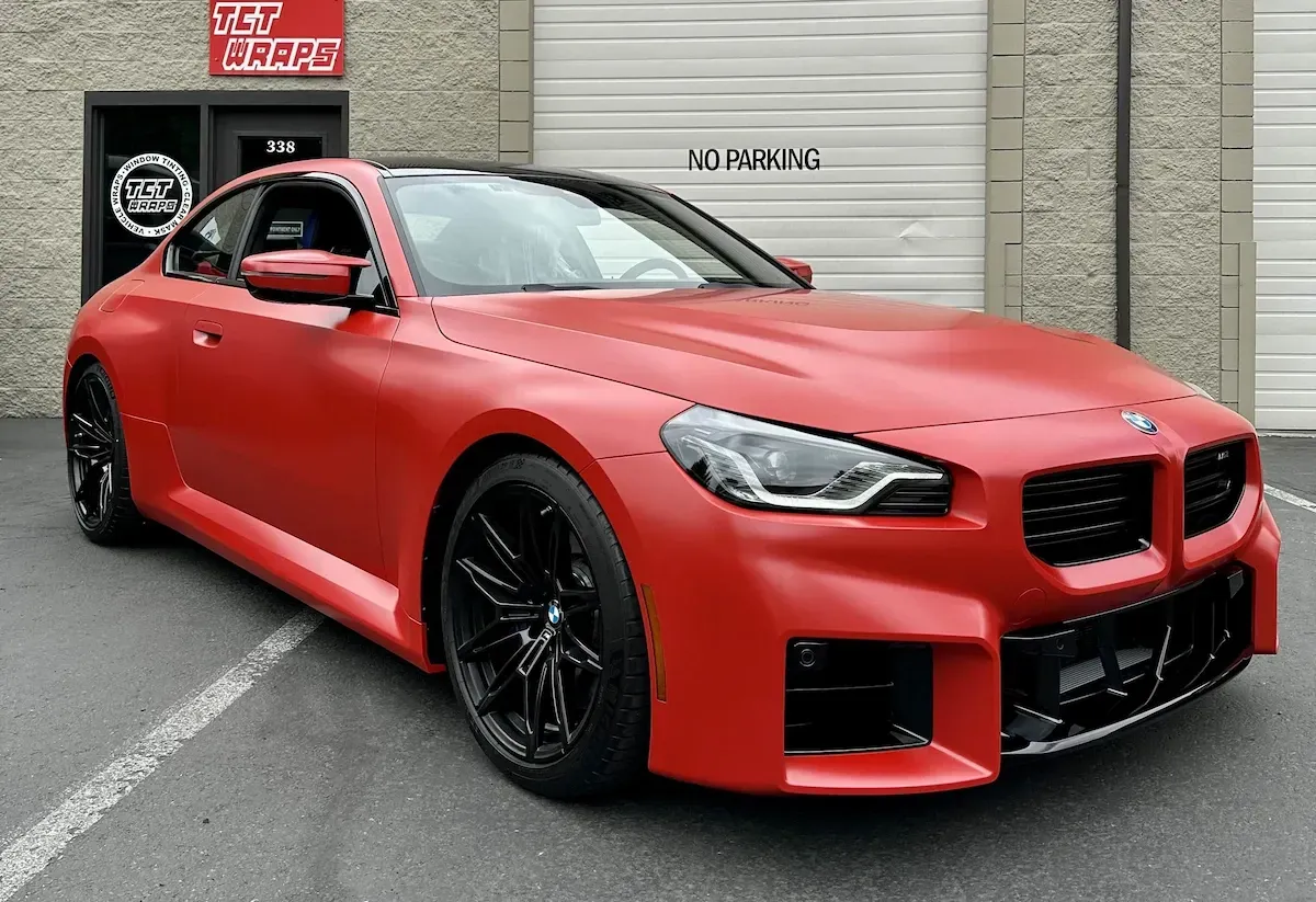 Red sports coupe with black wheels parked outside a building