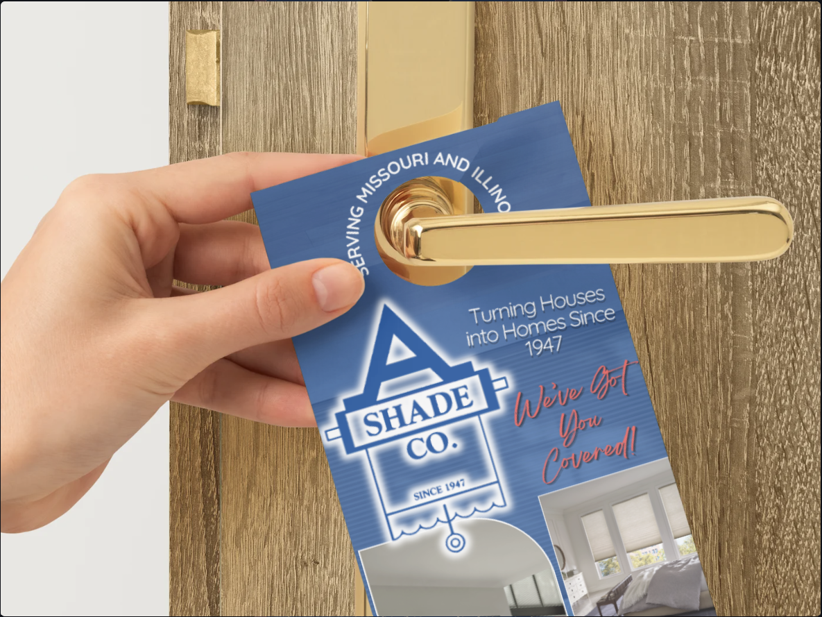 A hand hanging a blue A Shade Co. door hanger on a gold handle against a textured wood door.