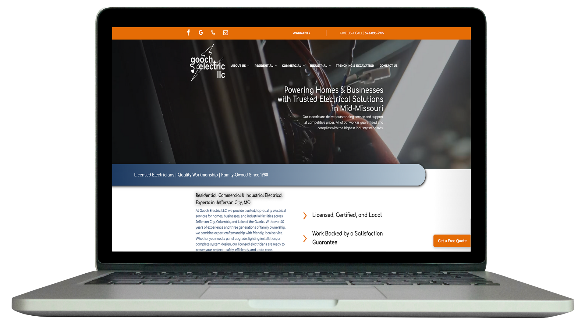 A silver laptop displaying a professional website with an orange header, dark navigation bar, and text.