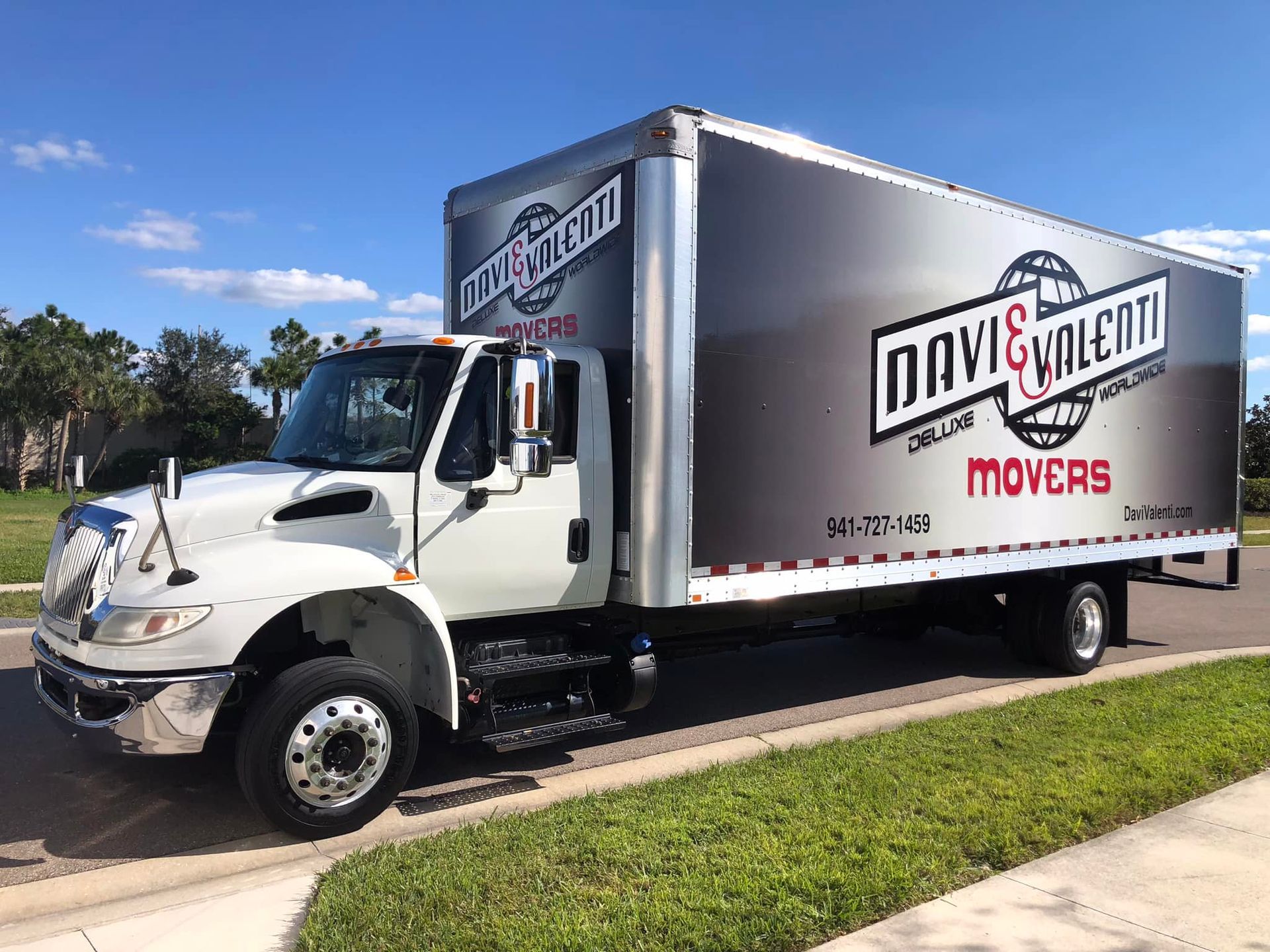 White and gray Davi & Valenti Movers truck parked on a street with a blue sky.