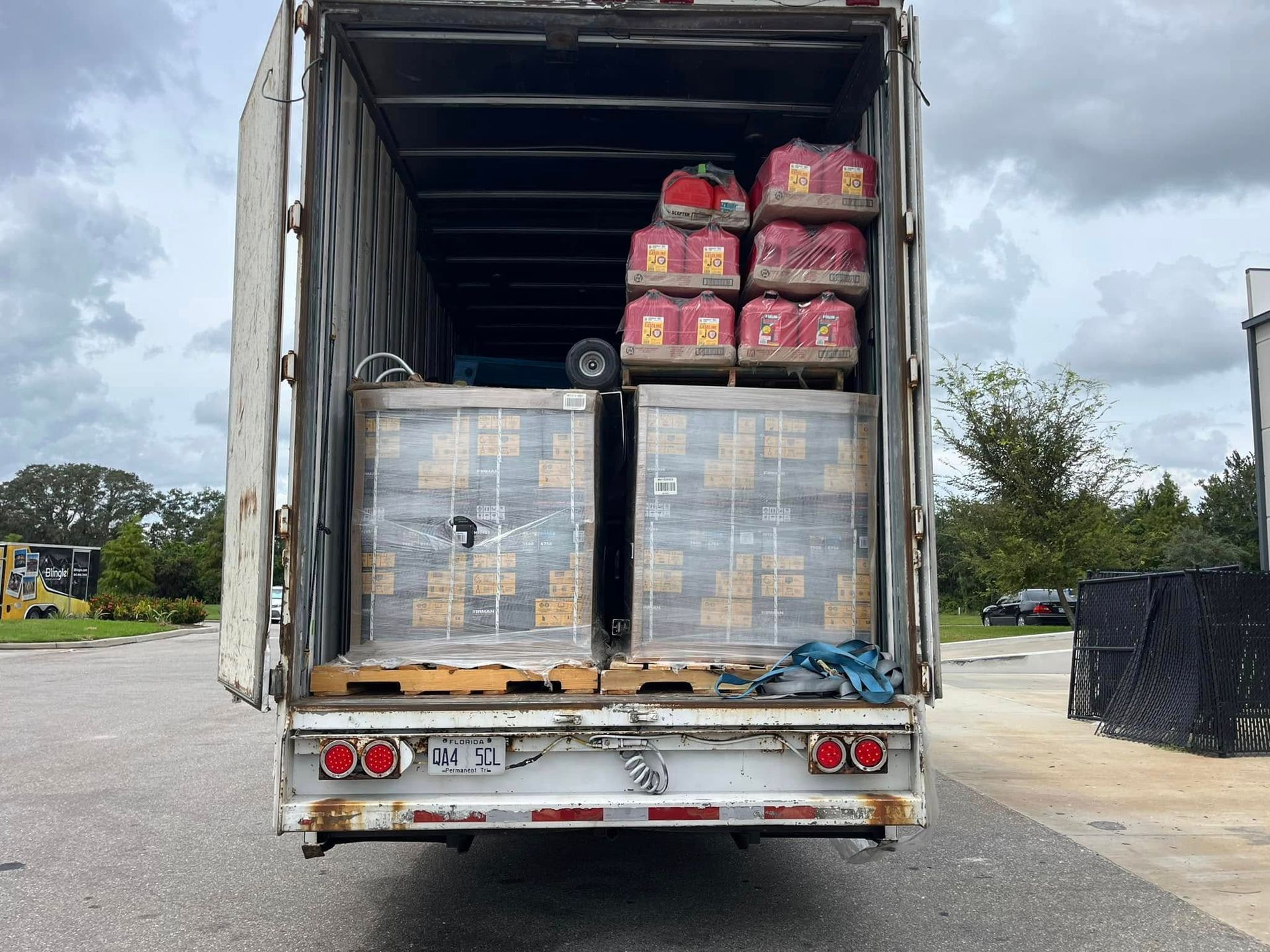 Open truck trailer loaded with pallets of packaged goods and stacks of red containers.