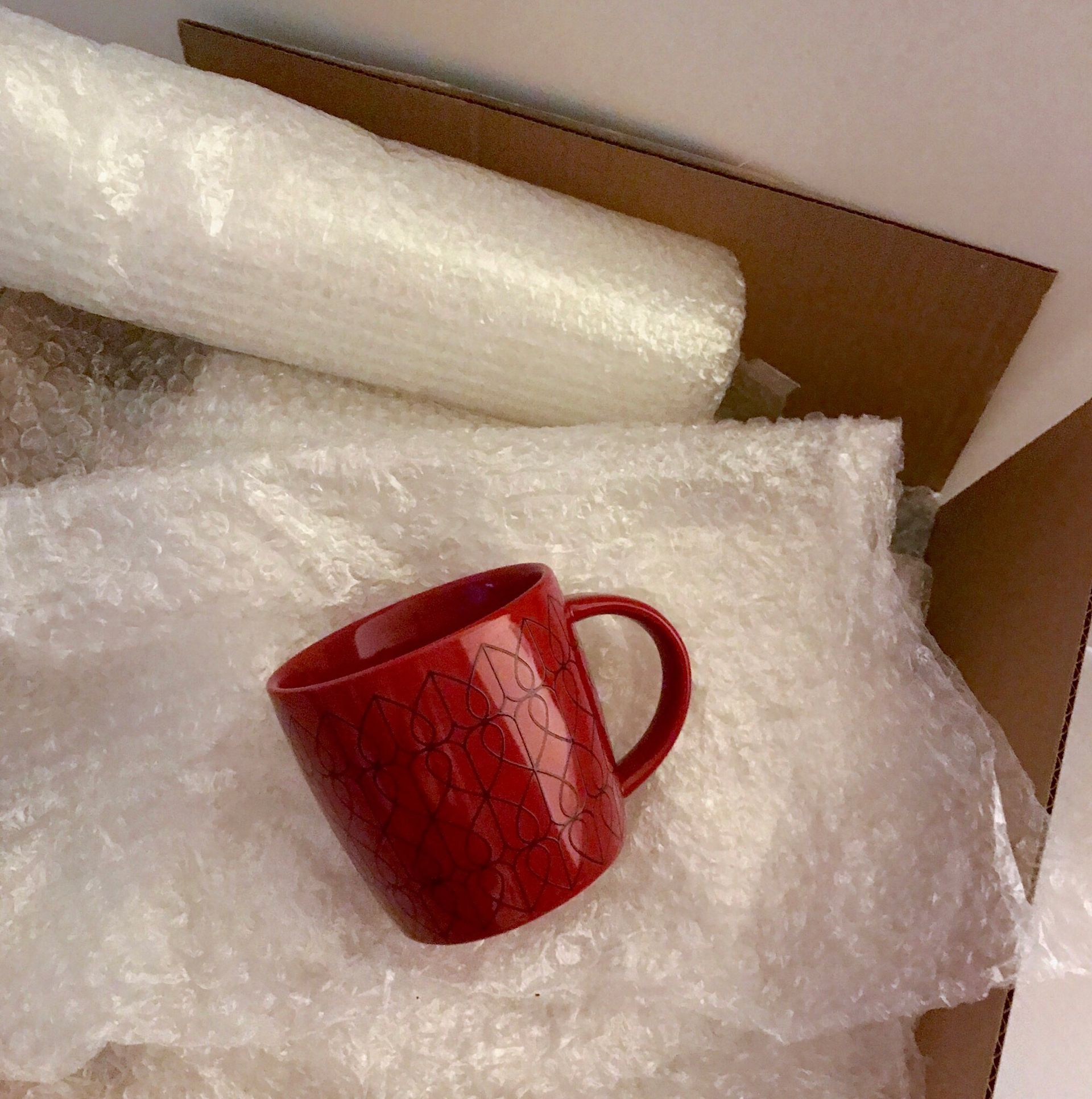 Red mug inside a cardboard box, surrounded by bubble wrap.