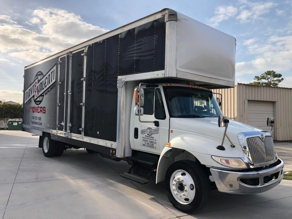 White moving truck parked outside a building. The truck has black panels with white text.