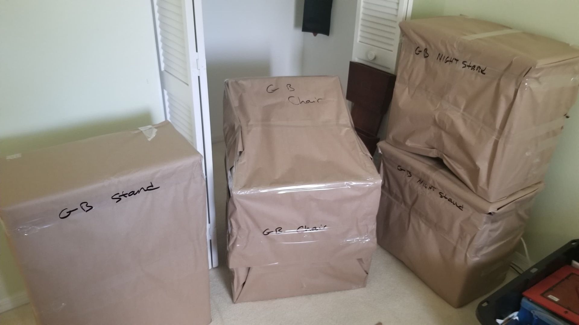 Boxes wrapped in brown paper and tape labeled with handwritten text. Stacked in a room, ready for moving.