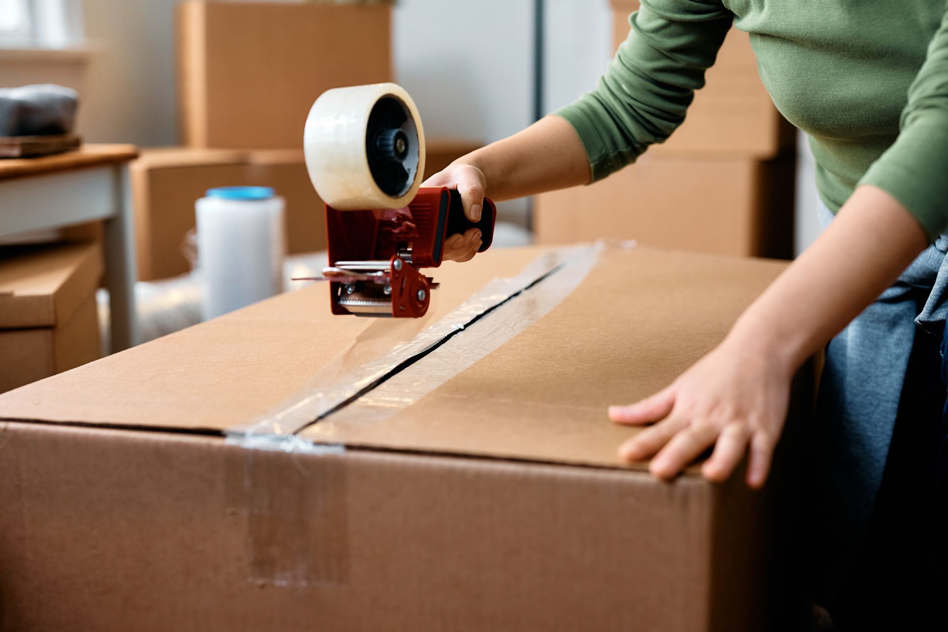 Person sealing a cardboard box with packing tape in a moving or shipping setup