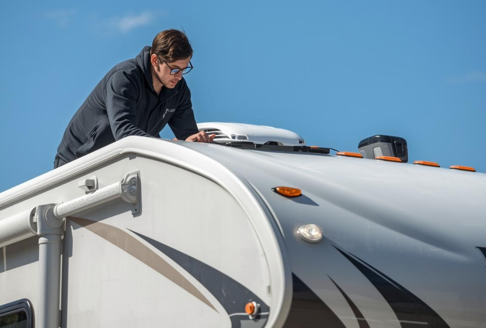 Man on RV roof inspecting equipment against a blue sky.