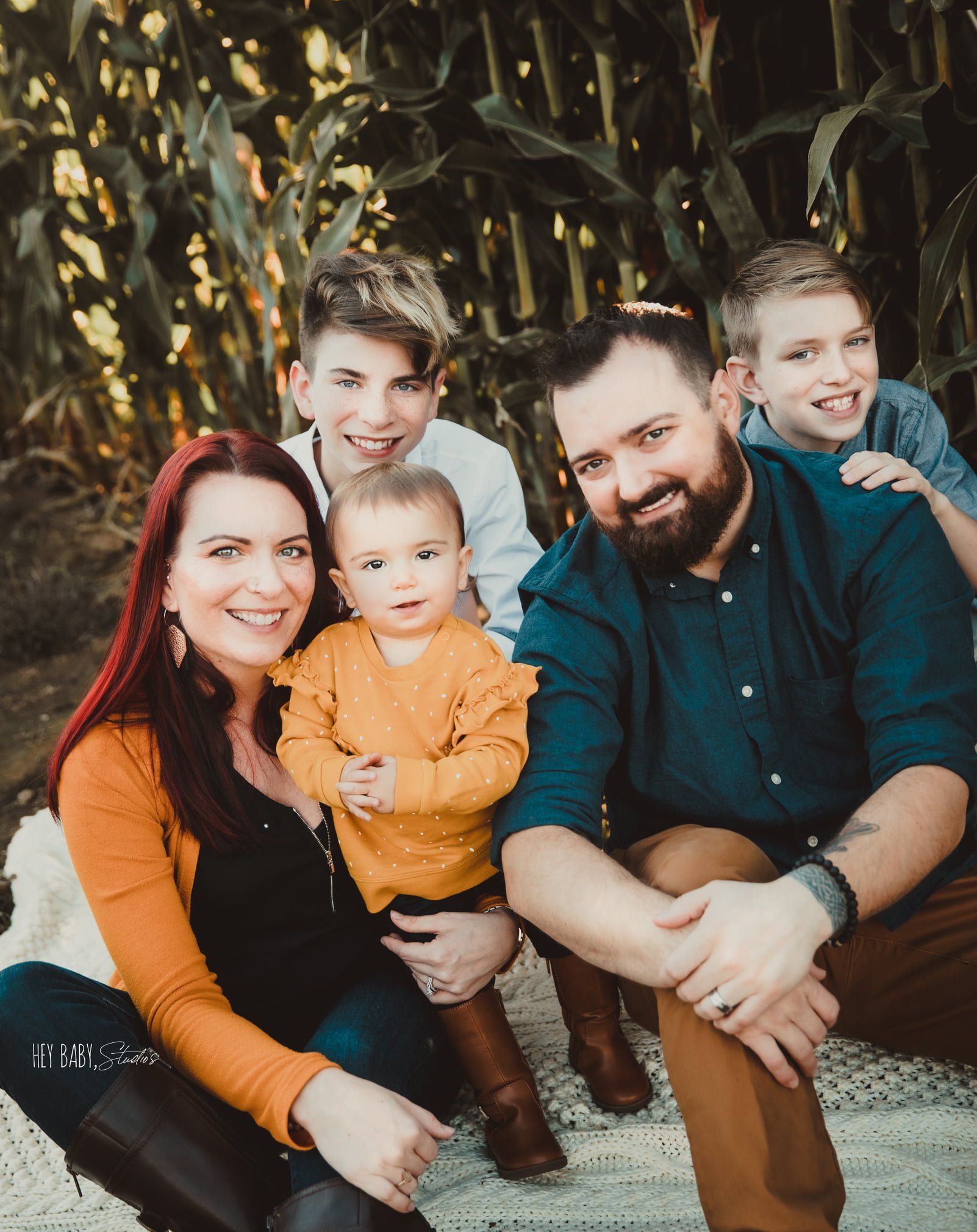 Family of five posing together in front of corn stalks; smiling.