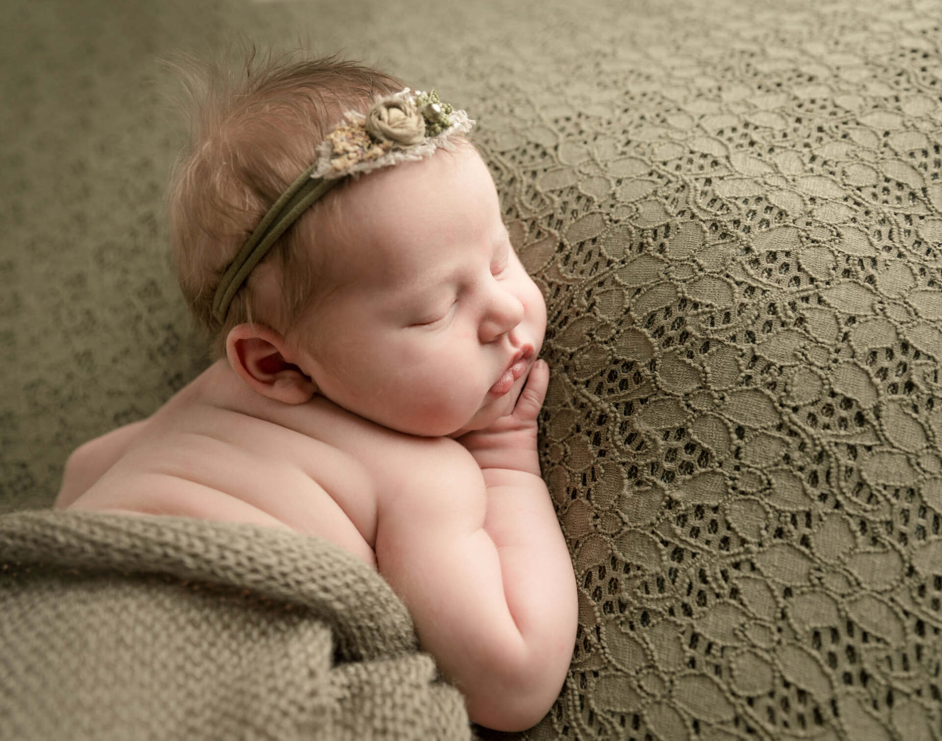 Sleeping baby wearing a floral headband, resting on a green knitted blanket.