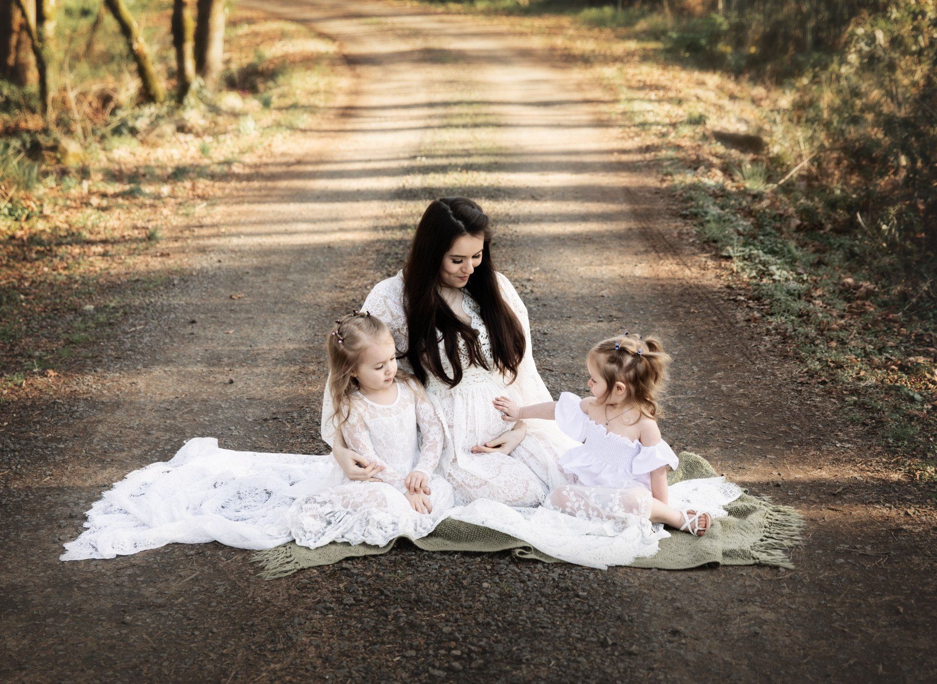 Woman and two young children sitting on a path. They wear white dresses.