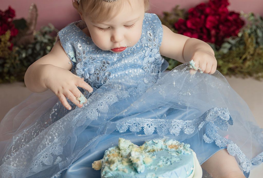 Young child in blue dress smashes a small cake.
