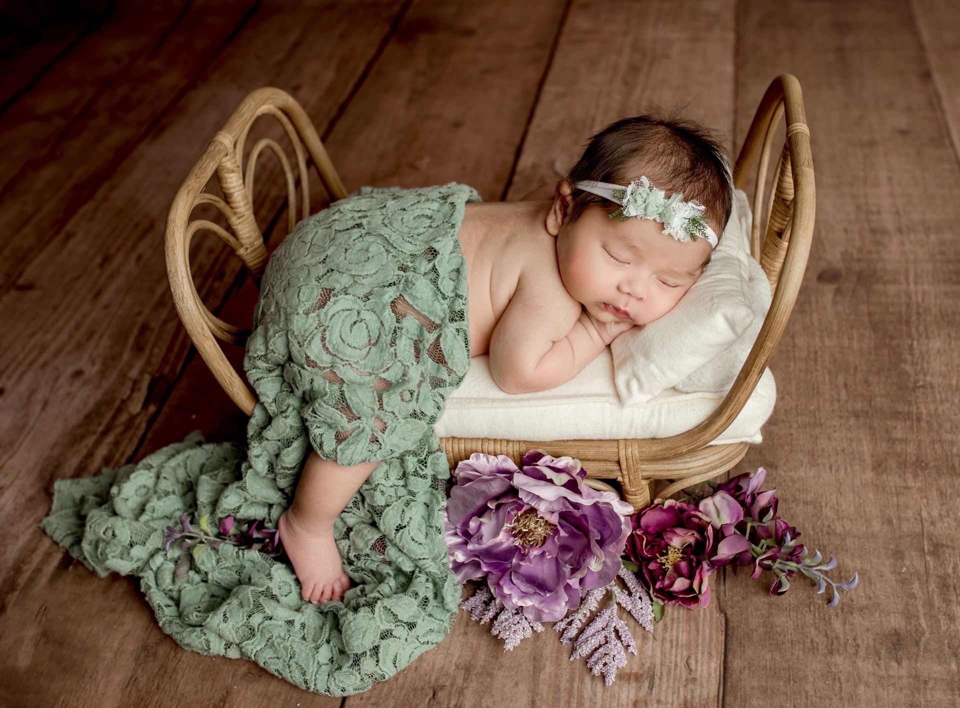 Newborn sleeping in a small, decorative wicker bed; wrapped in a green lace blanket.