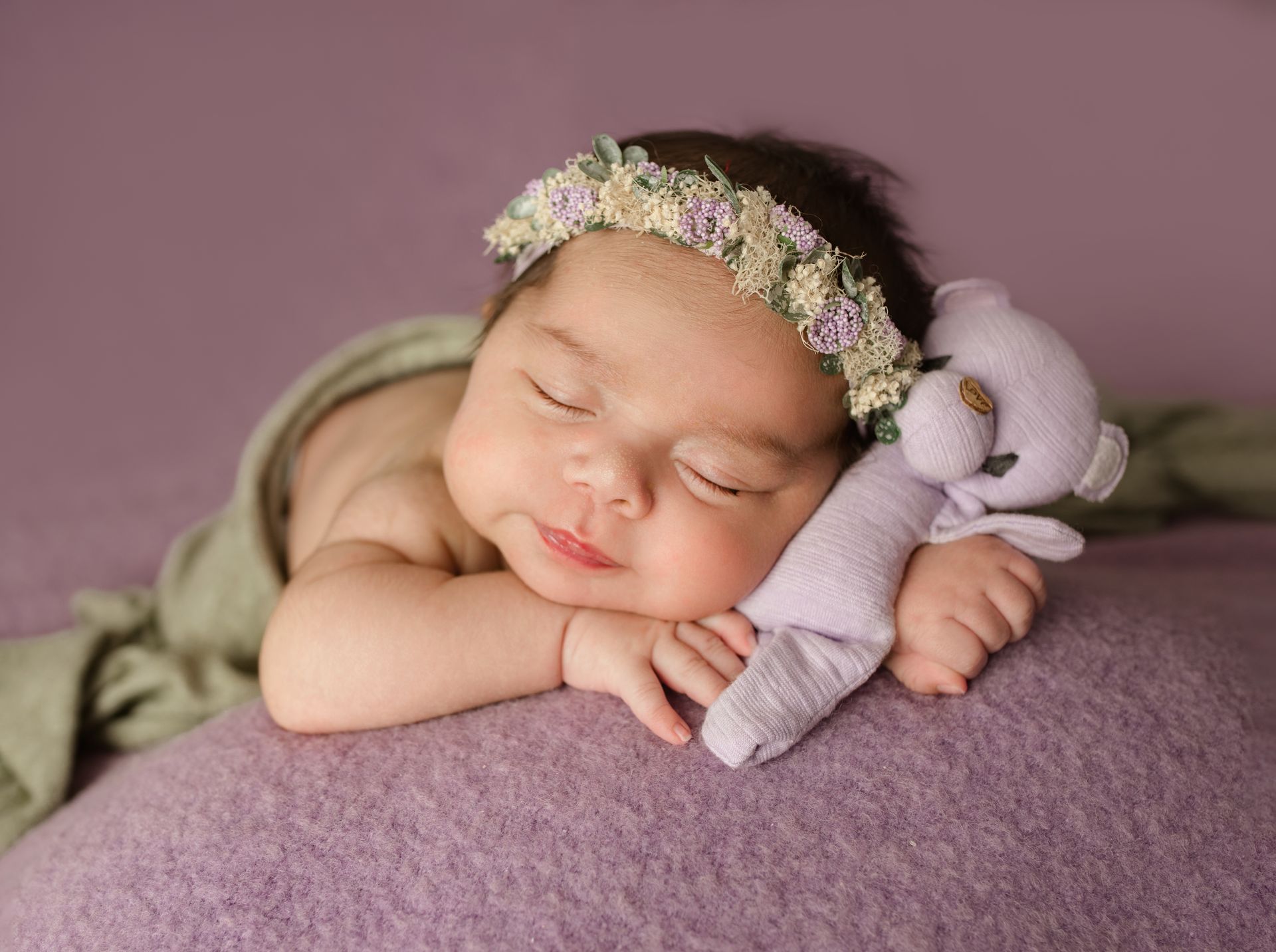 Sleeping baby with floral headband and purple stuffed toy.