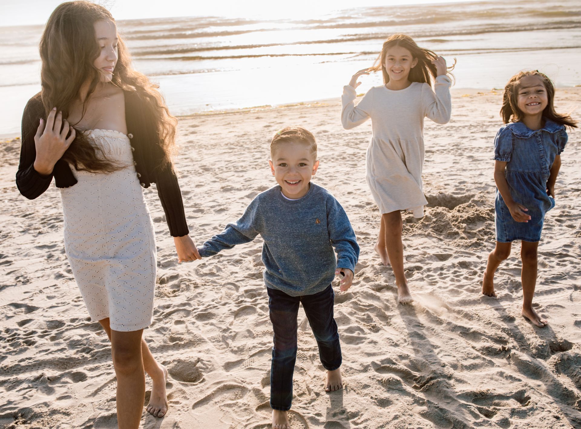 Four children walking on a beach, lit by sunlight.