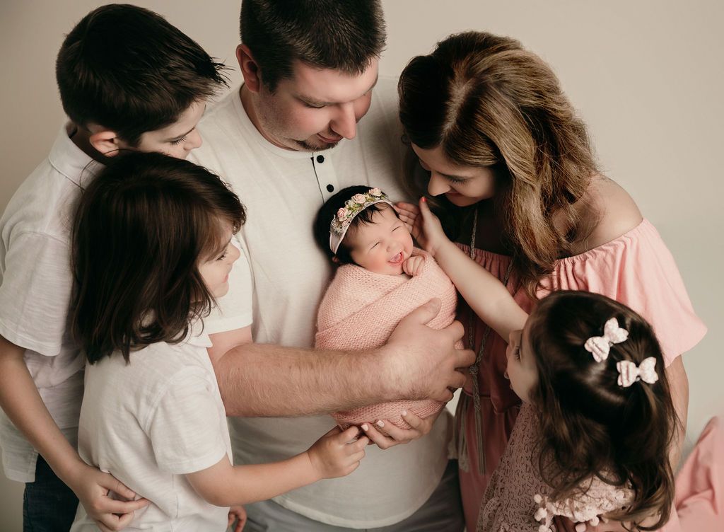 Family surrounded by newborn baby wrapped in pink blanket.