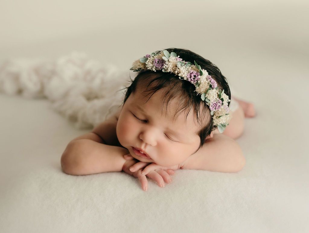 Newborn baby wearing a flower crown, lying peacefully on a soft blanket.