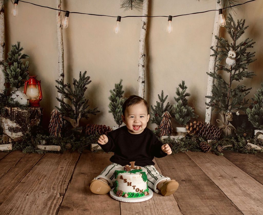 Boy smiles and reaches for cake in a forest-themed photo set.