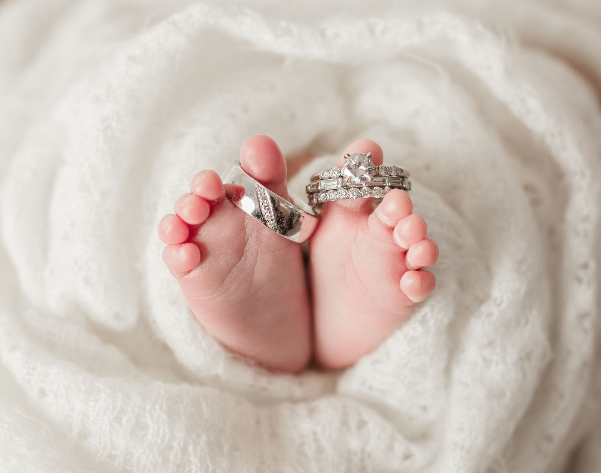 Baby's tiny feet nestled in white fabric, with two wedding rings resting on the toes.