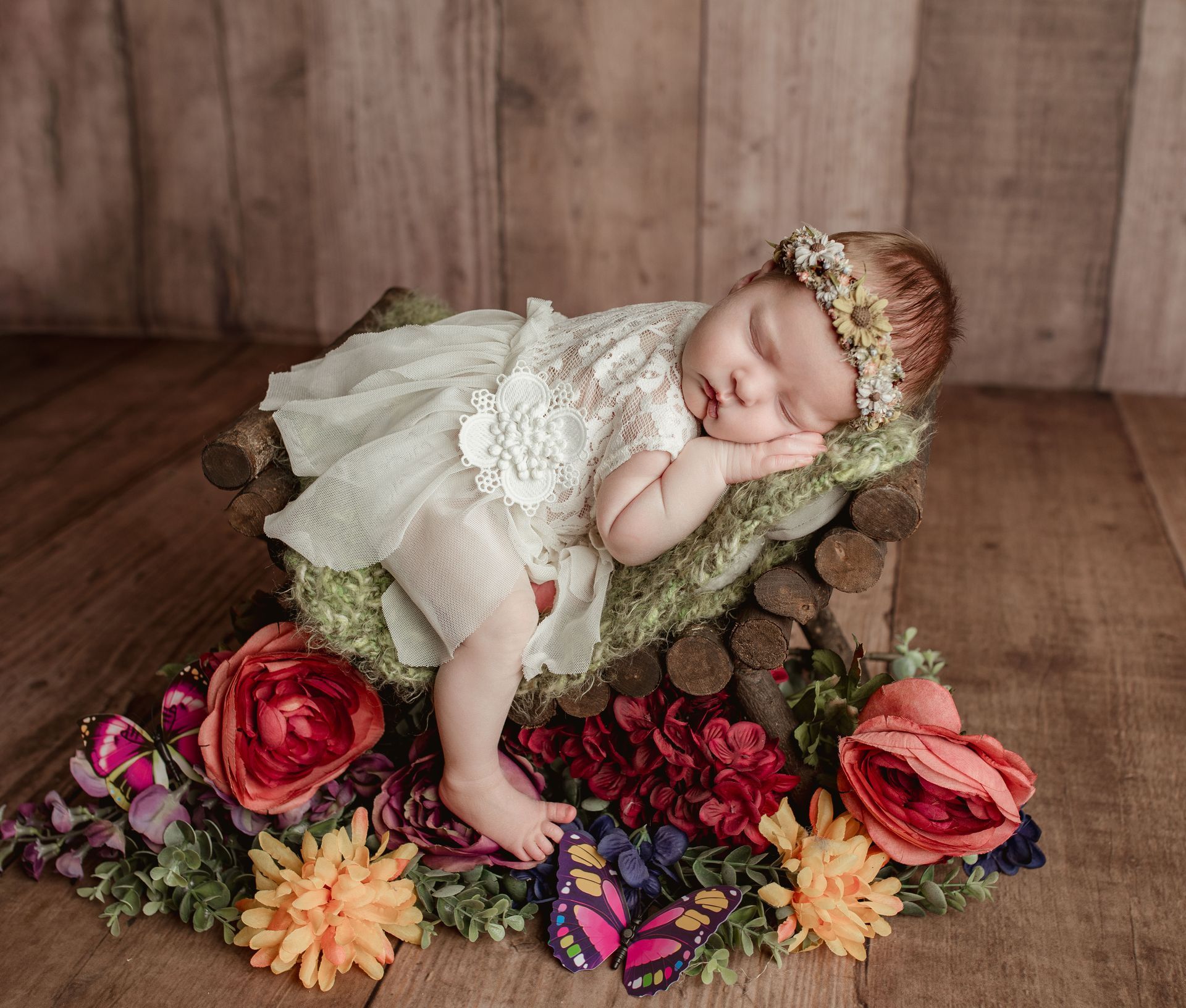 Newborn baby asleep in a wooden bed, adorned with flowers and a head wreath.