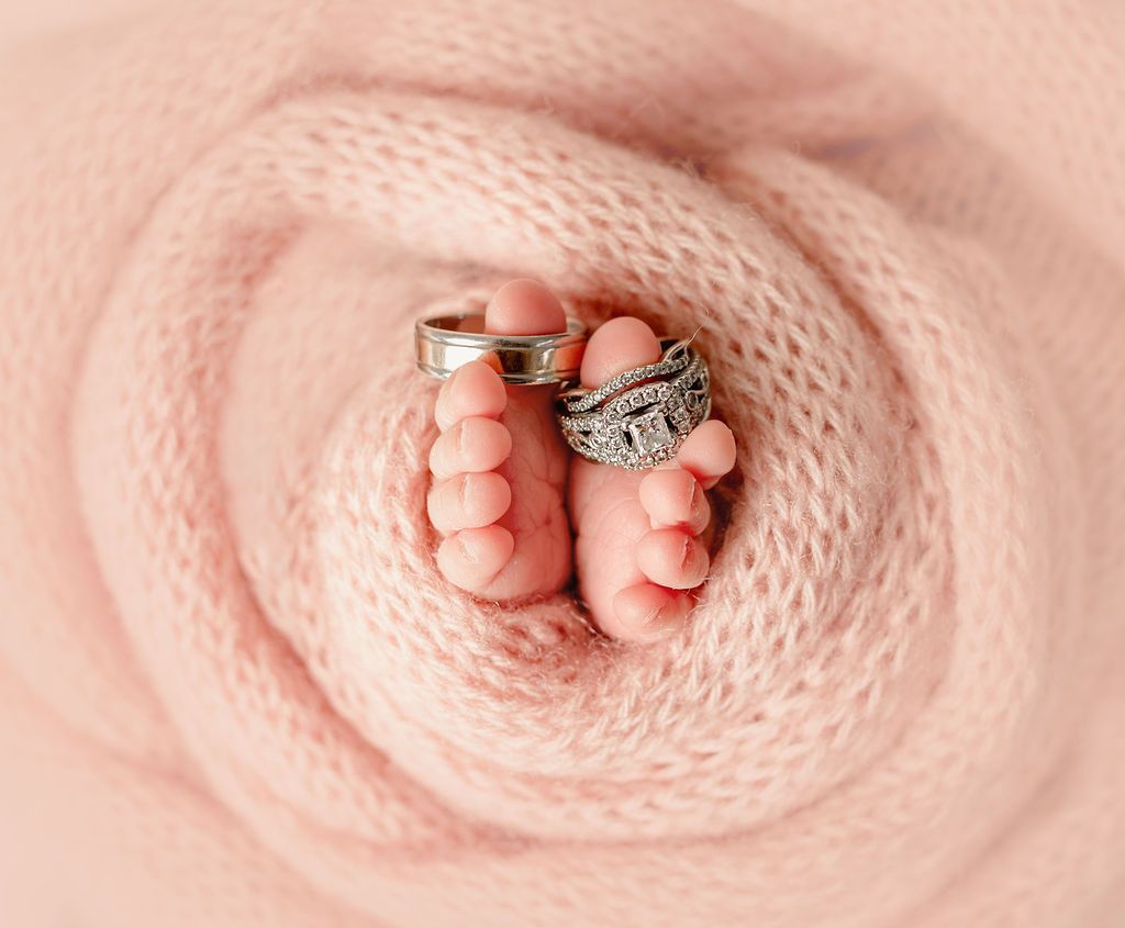 Baby feet with rings on toes, wrapped in pink fabric.