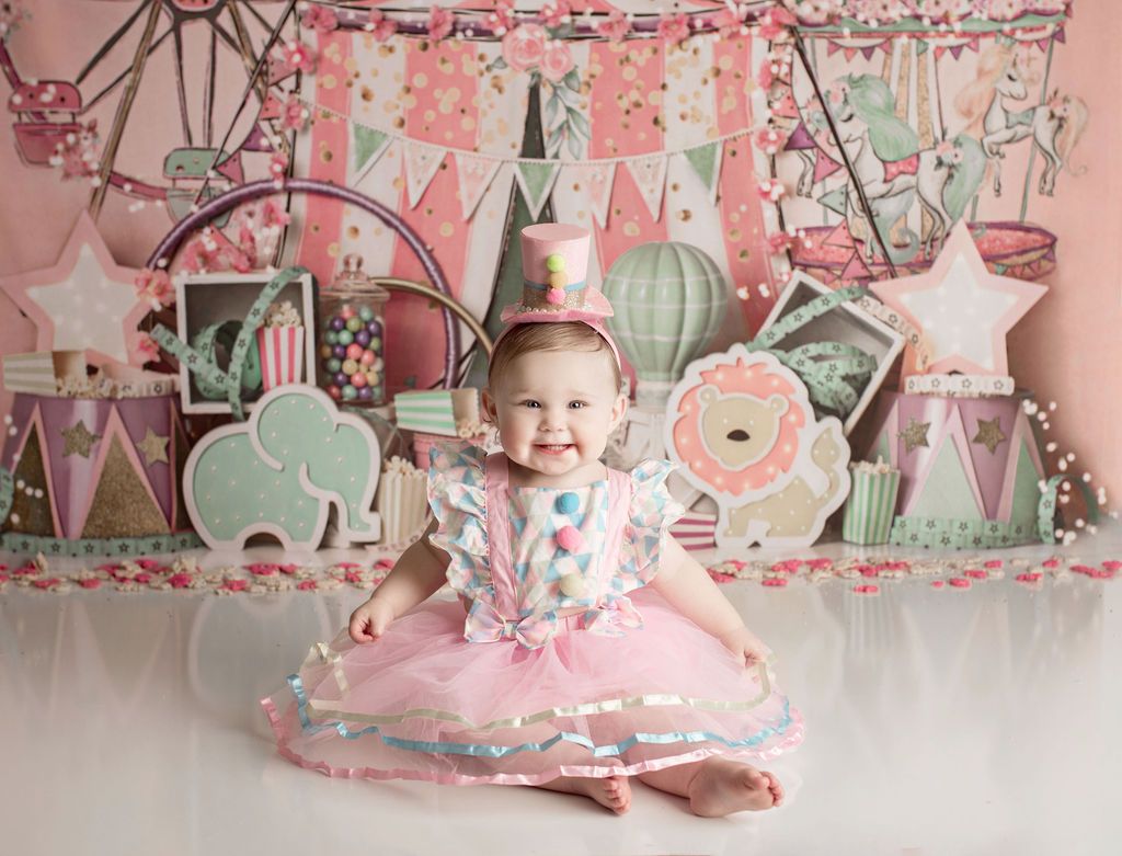 Child wearing circus-themed outfit smiles, sits in front of a colorful backdrop with circus decorations.