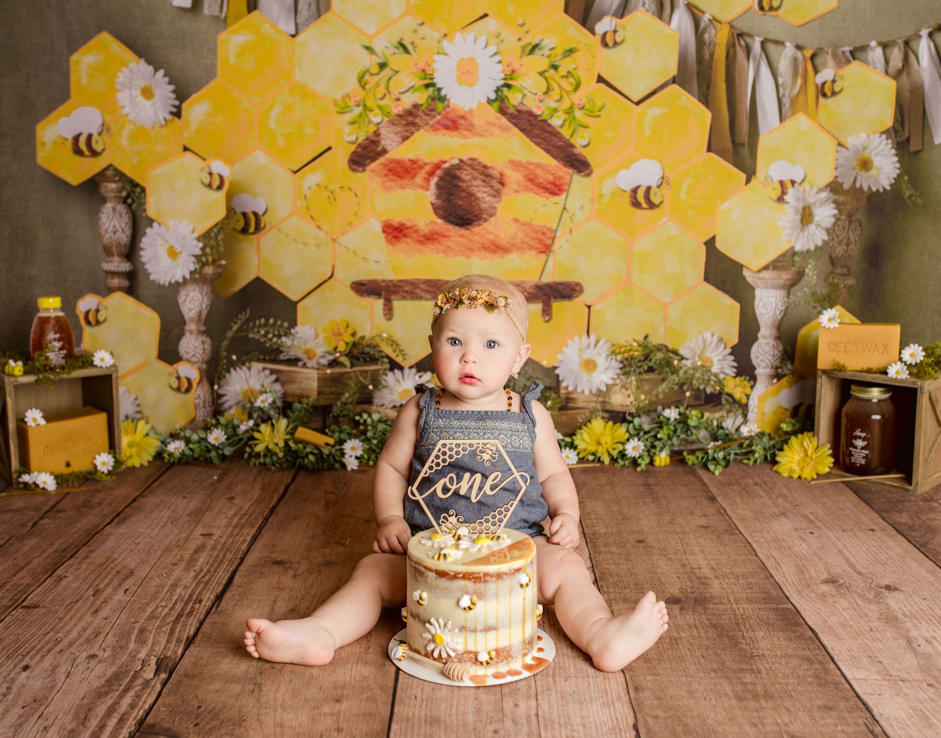 Baby sits in front of a bee-themed backdrop with cake.