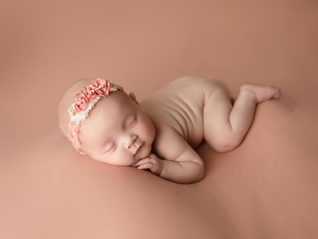 Sleeping newborn wearing a floral headband, lying on a pink blanket.
