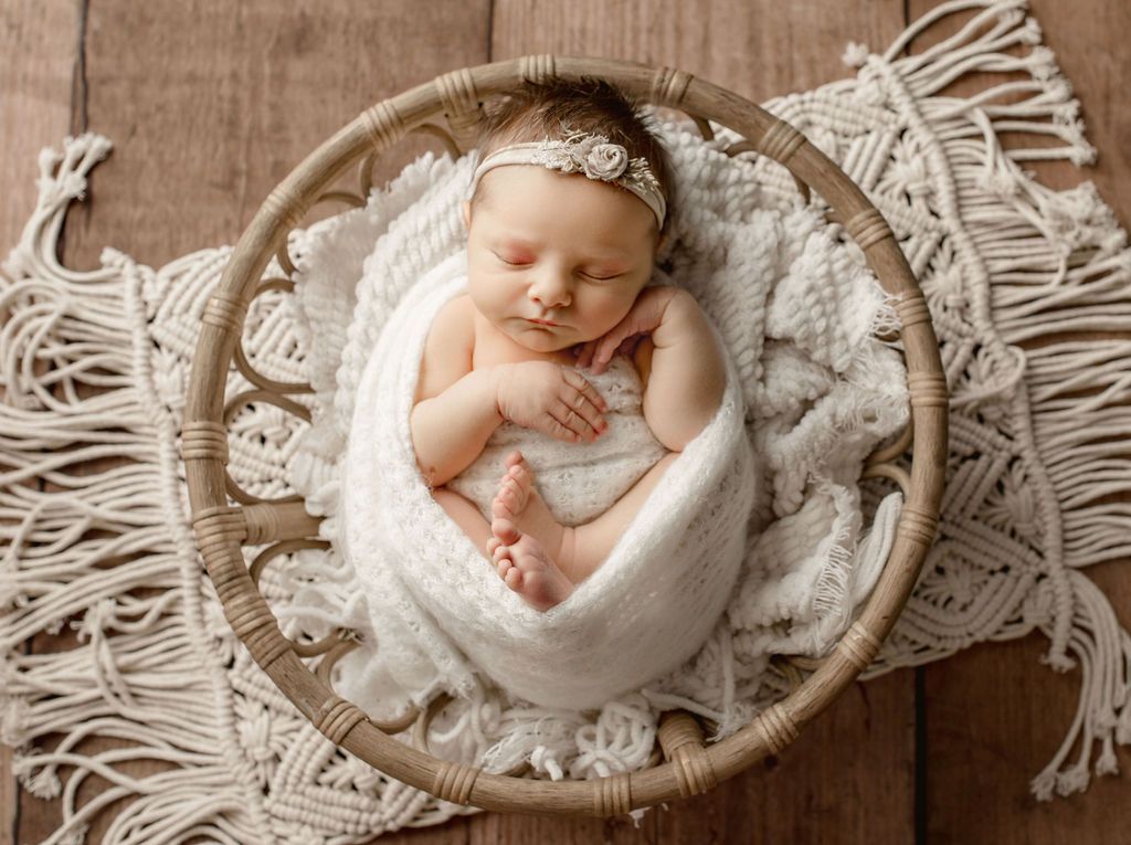 Newborn baby wrapped in white blanket, in a wicker basket, on macrame.