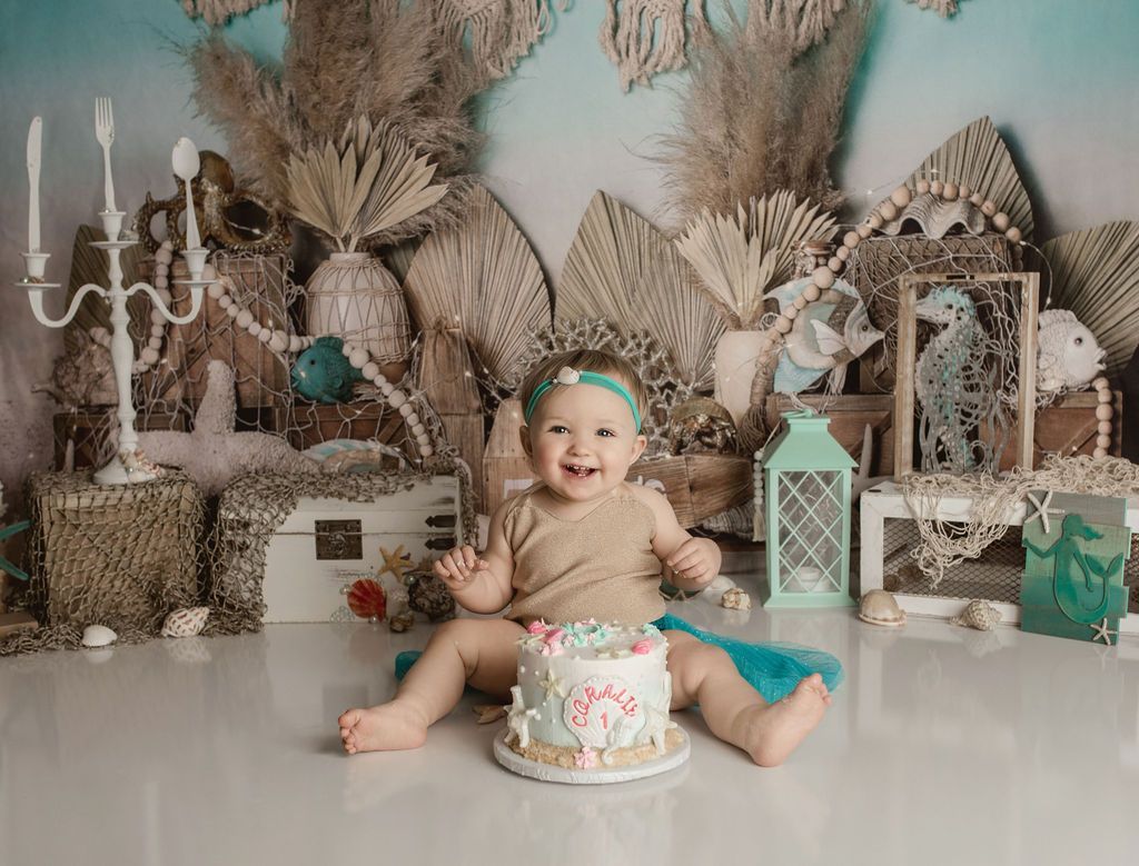 Smiling baby with a cake in front of an ocean-themed backdrop.
