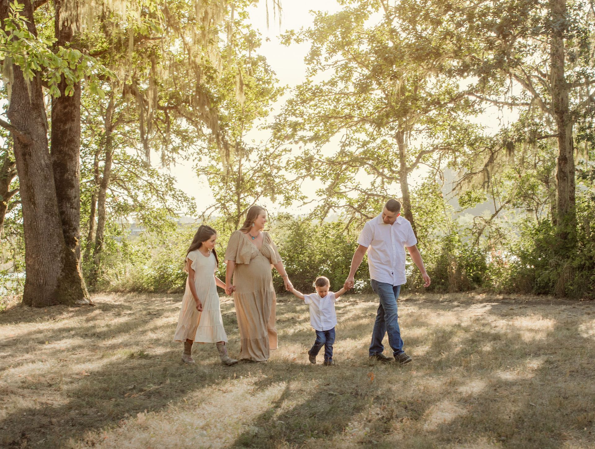 Family of four walking through a sunlit park, holding hands.