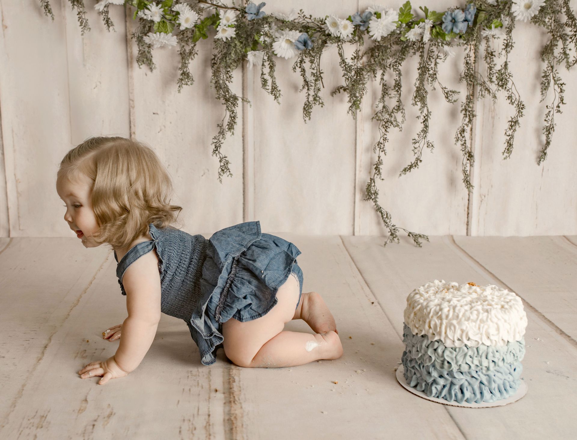 Baby crawling towards a blue and white cake; floral background.