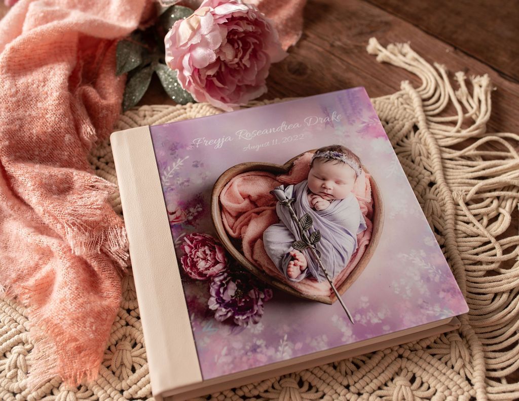 Newborn photo album with a baby in a heart-shaped bowl surrounded by pink flowers.
