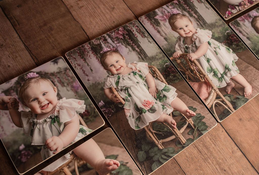 Baby in floral dress on wooden chairs and photo prints, smiles.