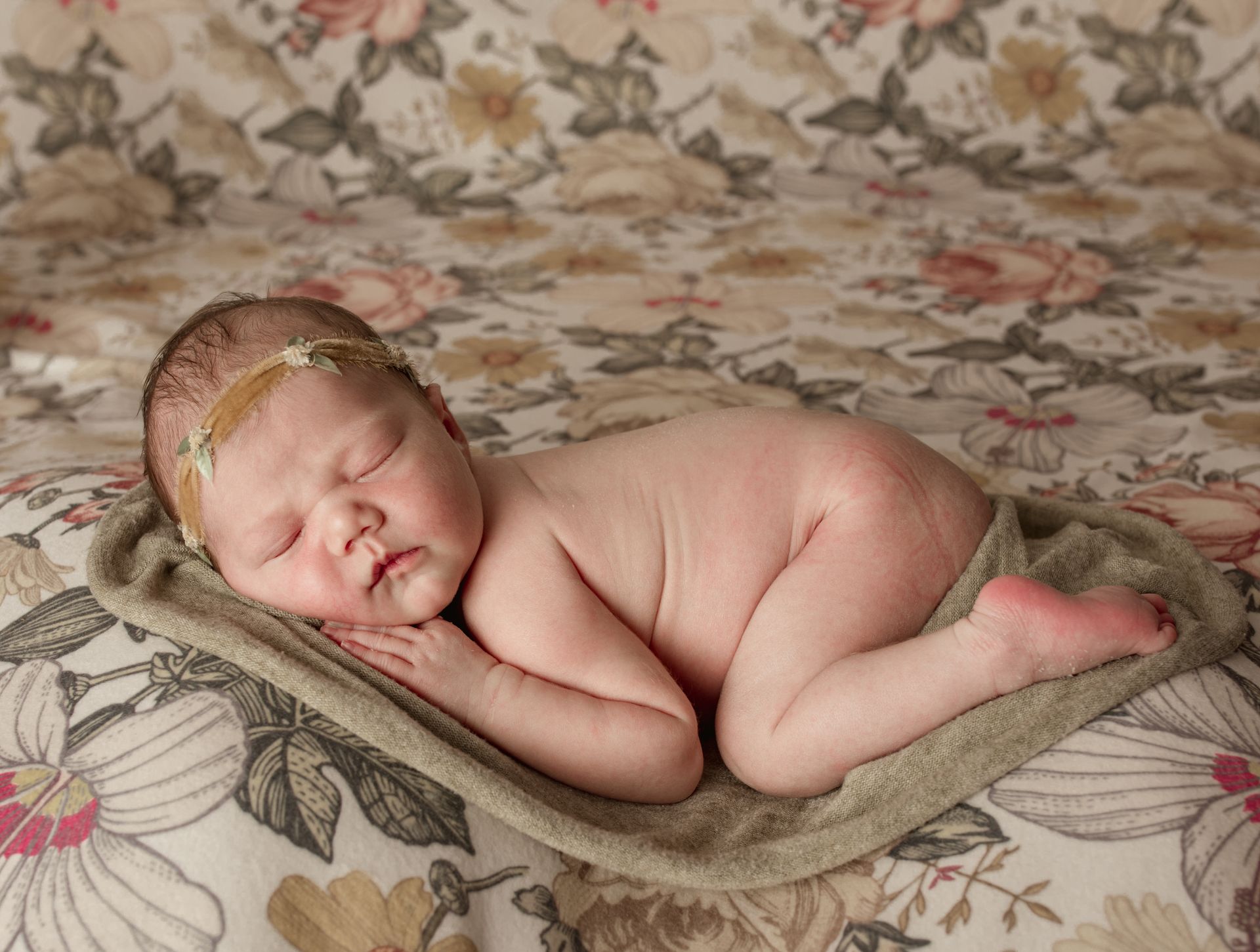 Sleeping newborn wearing a floral headband, curled on a towel, floral background.