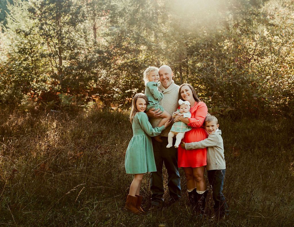Family of six smiling, posing outdoors in a field, surrounded by trees.