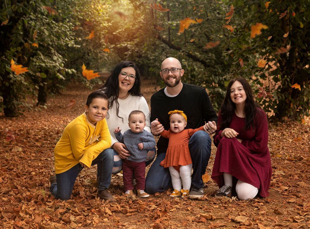 Family of six poses in a park, surrounded by falling autumn leaves.