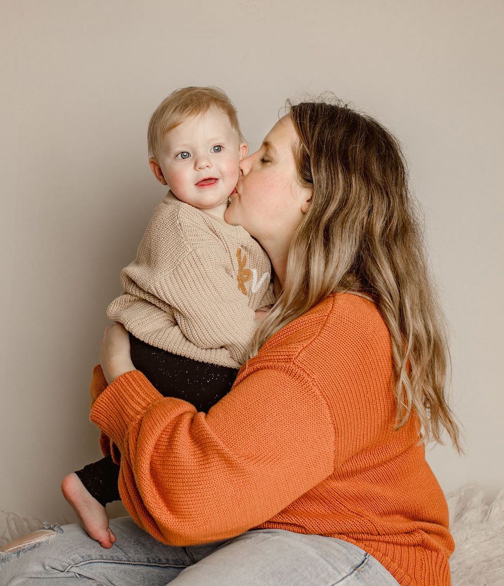 Woman kissing a child on the cheek. Child smiles, woman wears orange sweater.
